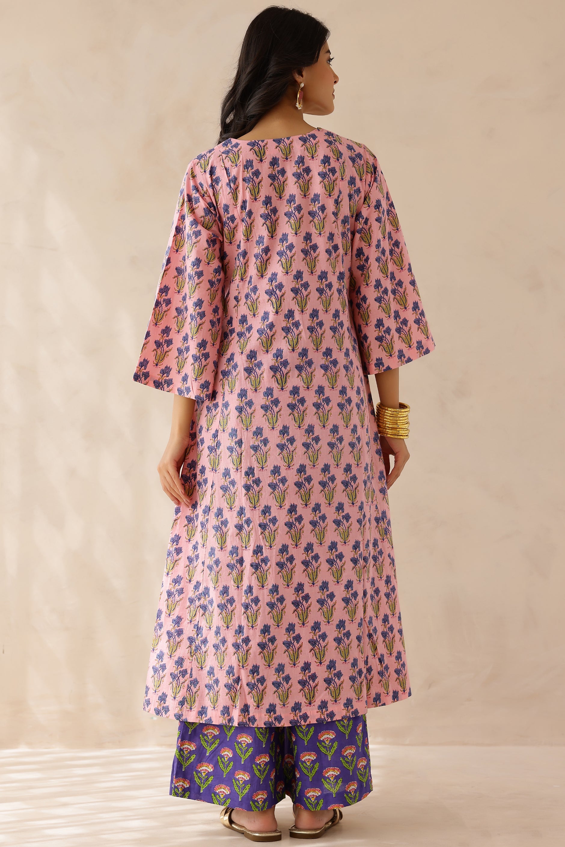 Woman wearing a pink printed cotton kurta with a V-neckline and 3/4th sleeves, paired with purple printed palazzo pants and a contrasting kota doria dupatta