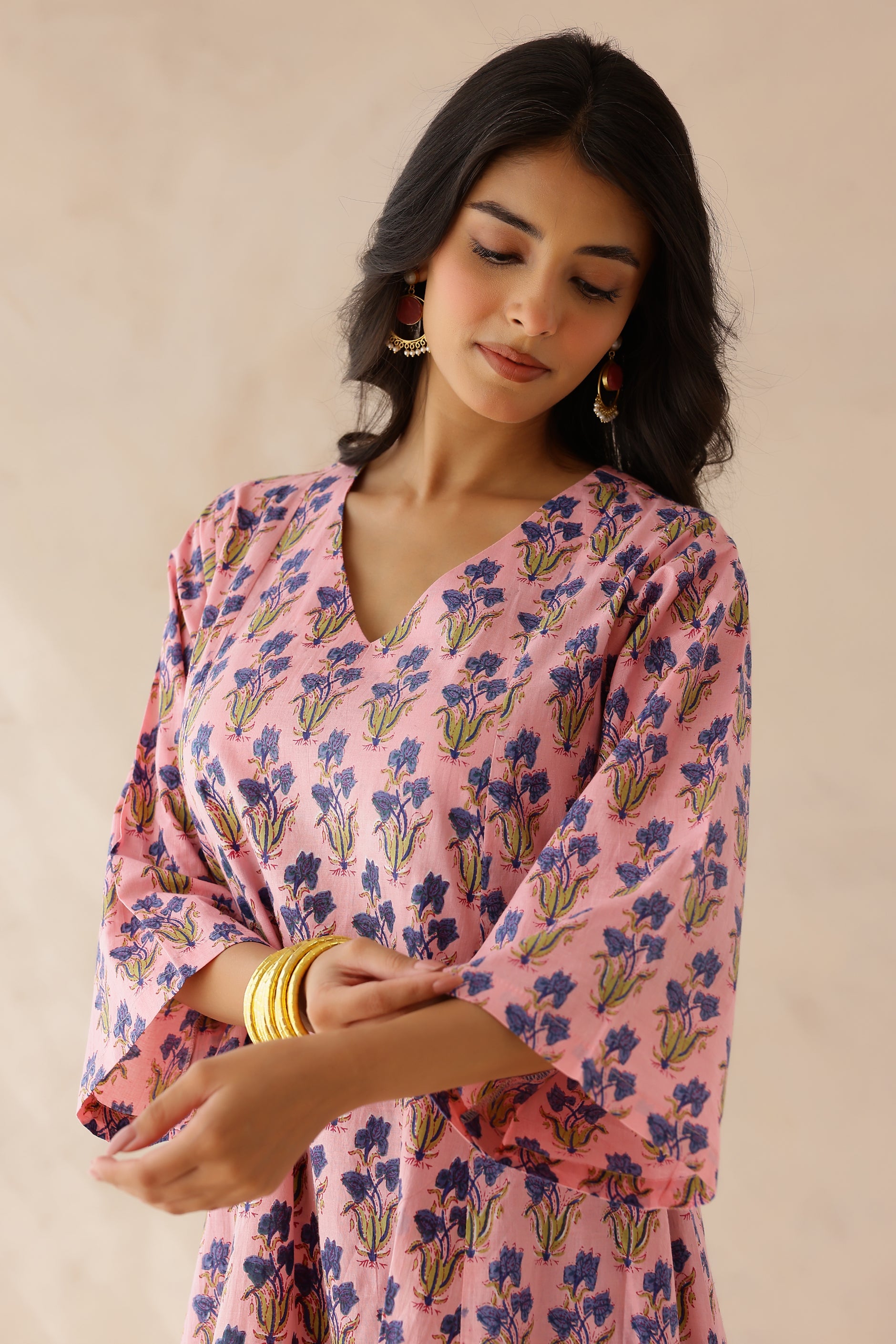 Woman wearing a pink printed cotton kurta with a V-neckline and 3/4th sleeves, paired with purple printed palazzo pants and a contrasting kota doria dupatta