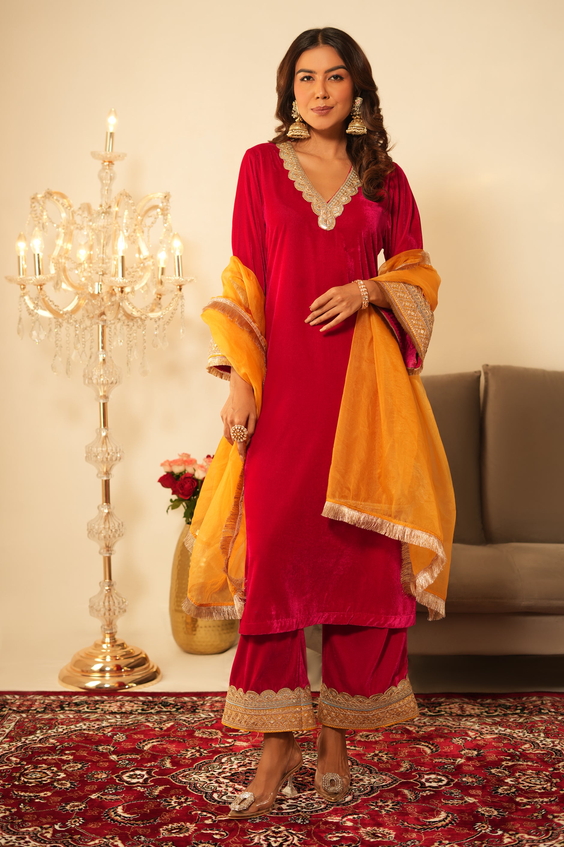 Woman wearing Pink Velvet Suit with Mustard Organza Dupatta 3 piece set featuring contrast lace detailing on neckline, sleeves and pant hem, V neckline, full sleeves, matching pink velvet pants with elastic waist, and sheer mustard organza dupatta