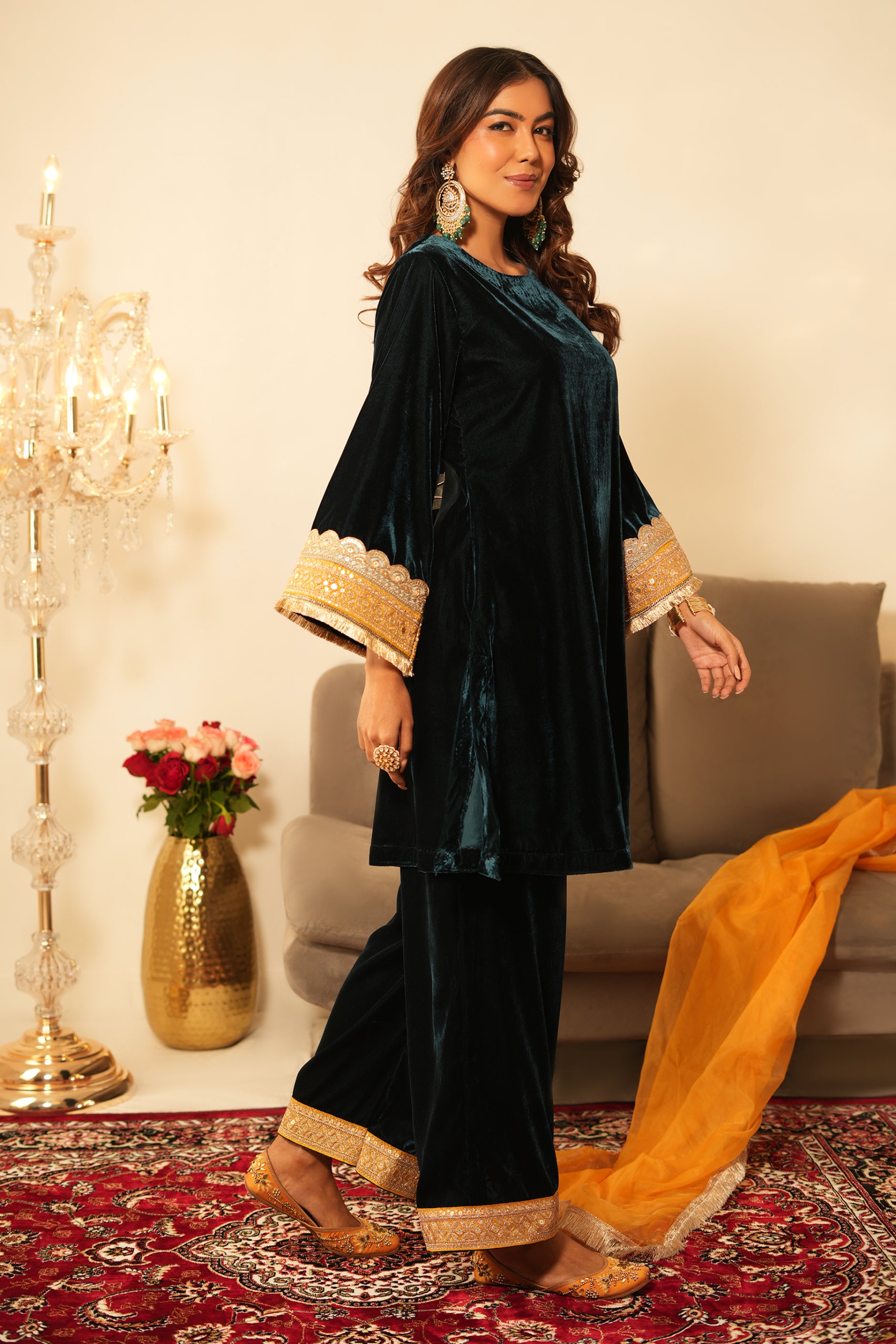 Woman wearing Blue Velvet Co-Ord Set featuring gota lace detailing on sleeves and hem, boat neckline, full sleeves, and matching green velvet pants with elastic waist and lace hem detailing