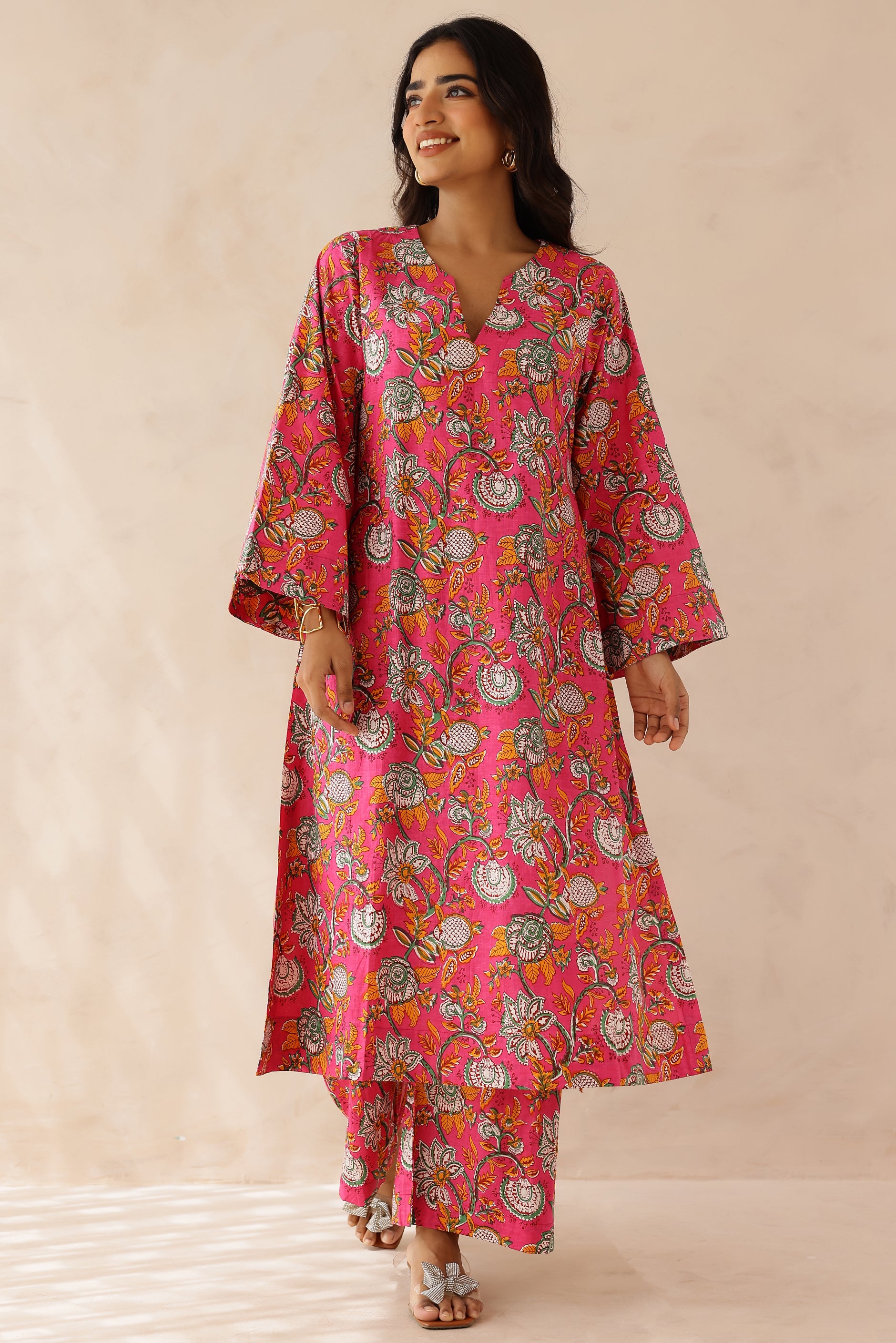 Woman wearing Pink Printed Cotton Kurta with Palazzo Set of 2 in light pink featuring all over prints, round to V neckline, full sleeves, and matching printed palazzo with elastic waist