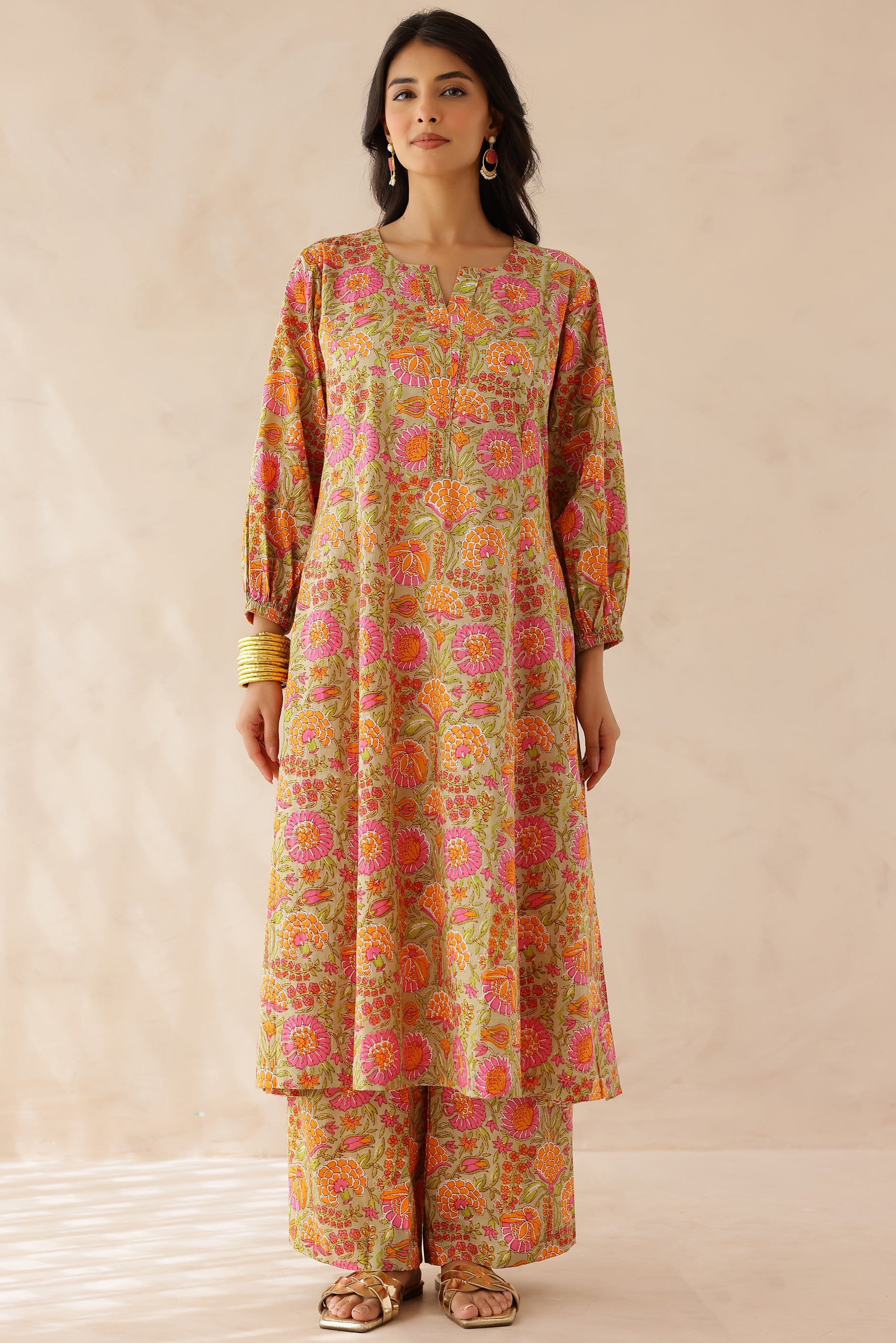 Woman wearing orange and pink printed cotton kurta with round V-cut neckline, 3/4 sleeves, and matching printed palazzo.