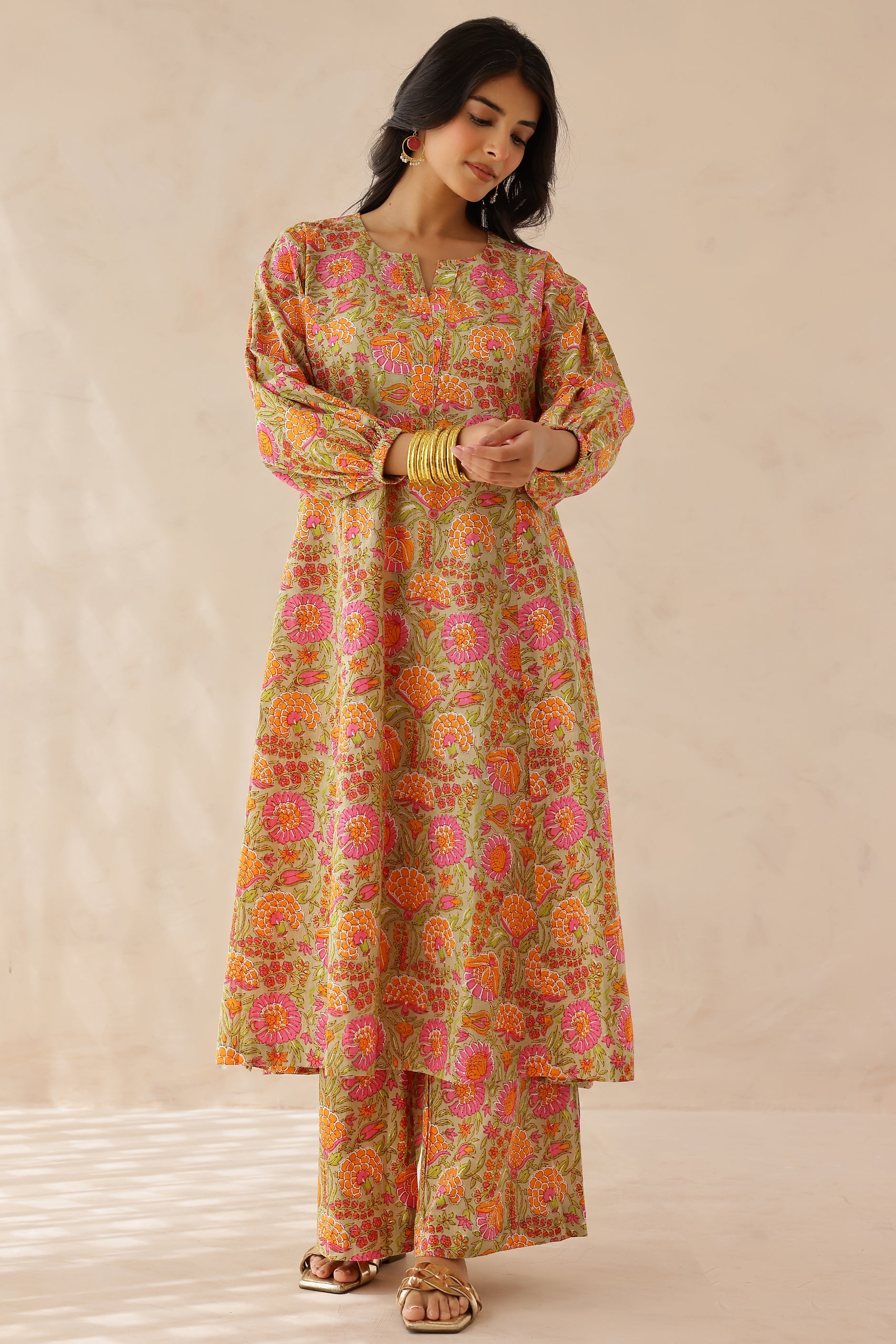 Woman wearing orange and pink printed cotton kurta with round V-cut neckline, 3/4 sleeves, and matching printed palazzo.