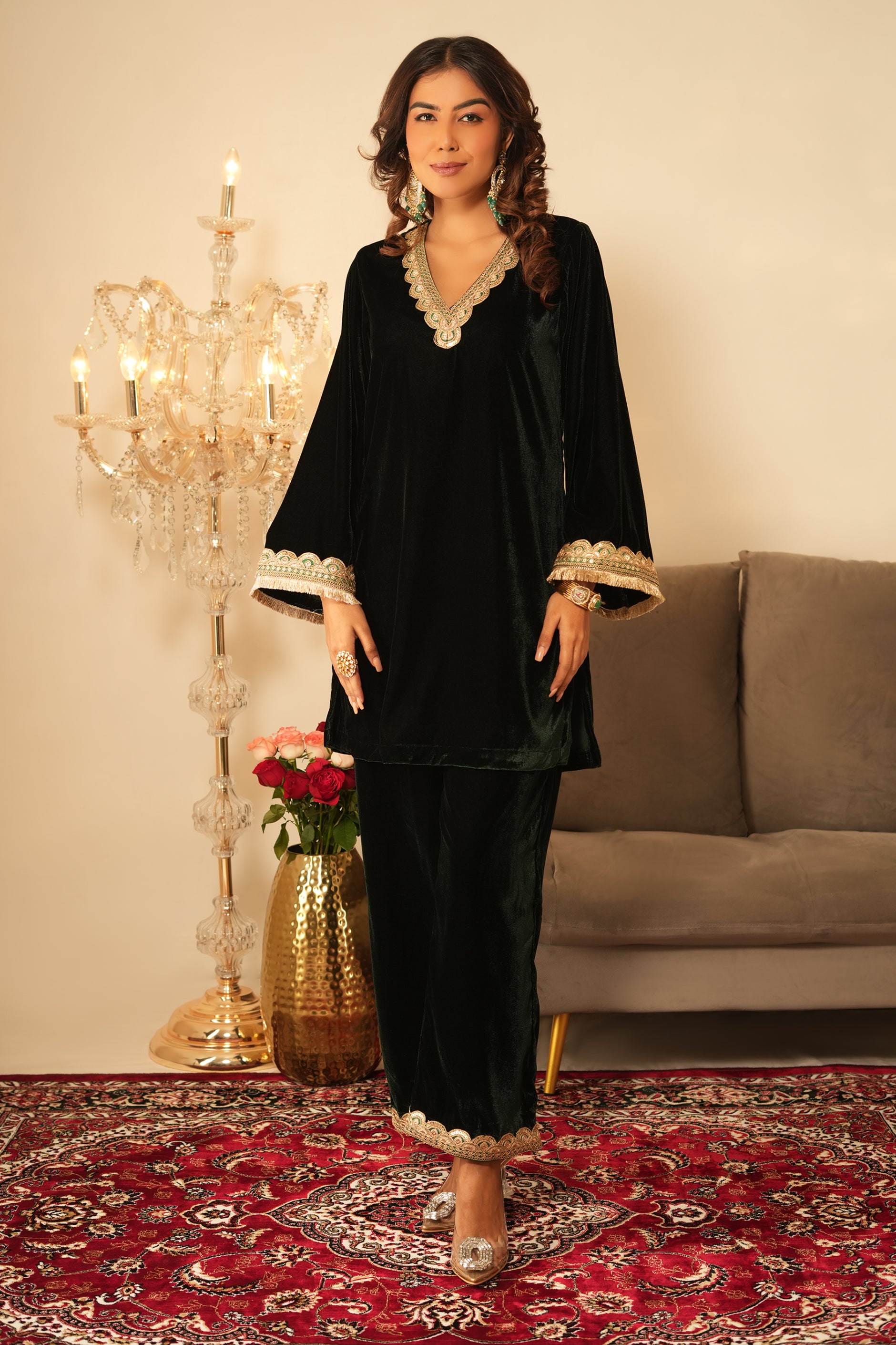 Woman in a traditional dark green velvet kurta outfit with gold accents standing in a decorated room 