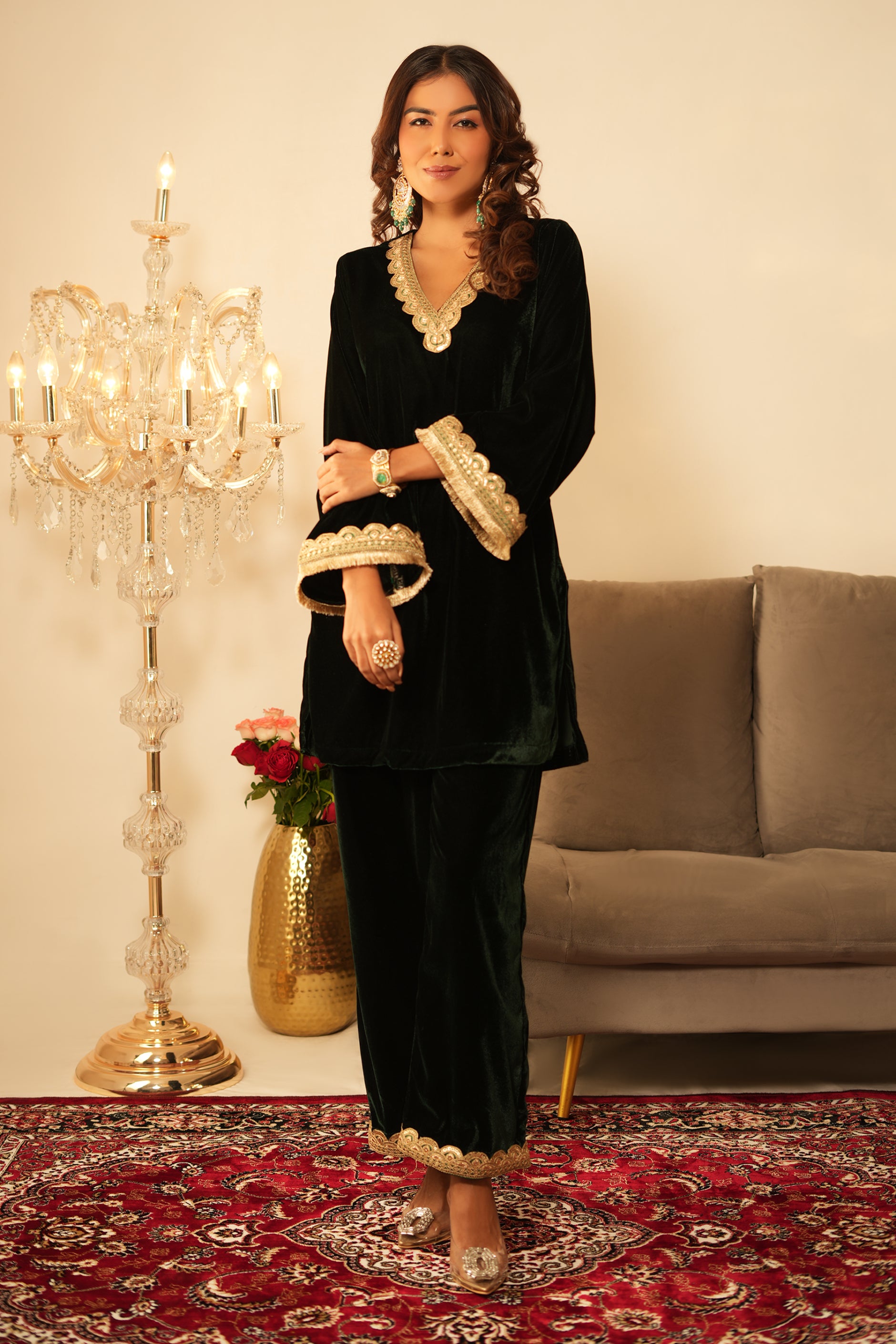 Woman in a traditional dark green velvet kurta outfit with gold accents standing in a decorated room 