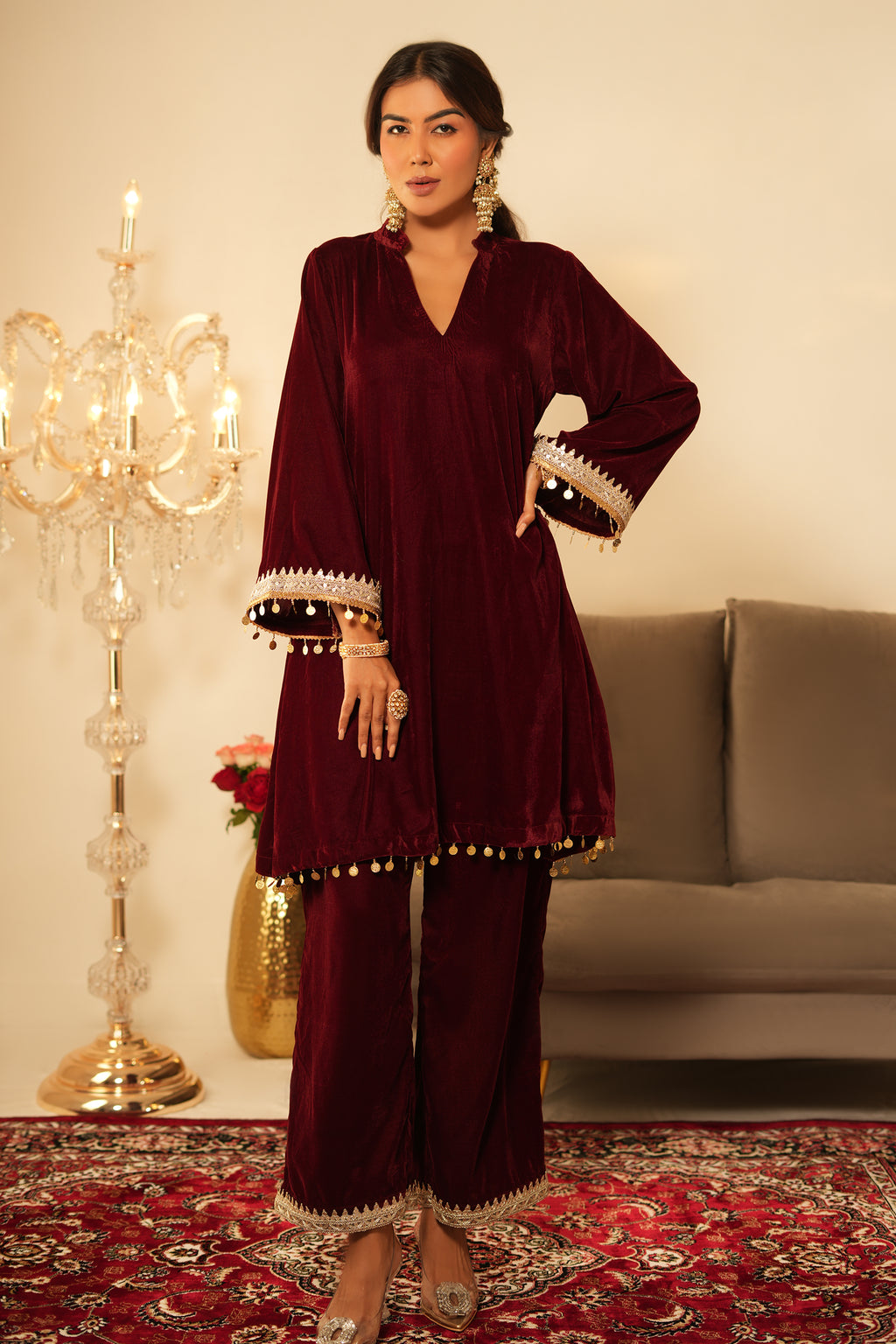 Woman in a maroon traditional outfit standing on a patterned rug with decorative elements.