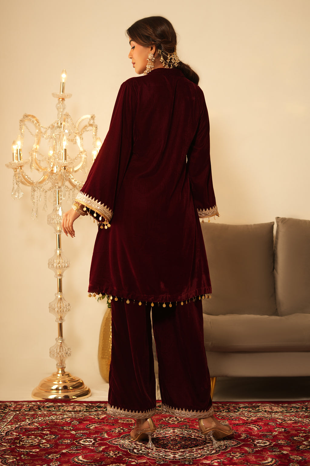 Woman in a maroon traditional outfit standing on a patterned rug with decorative elements.