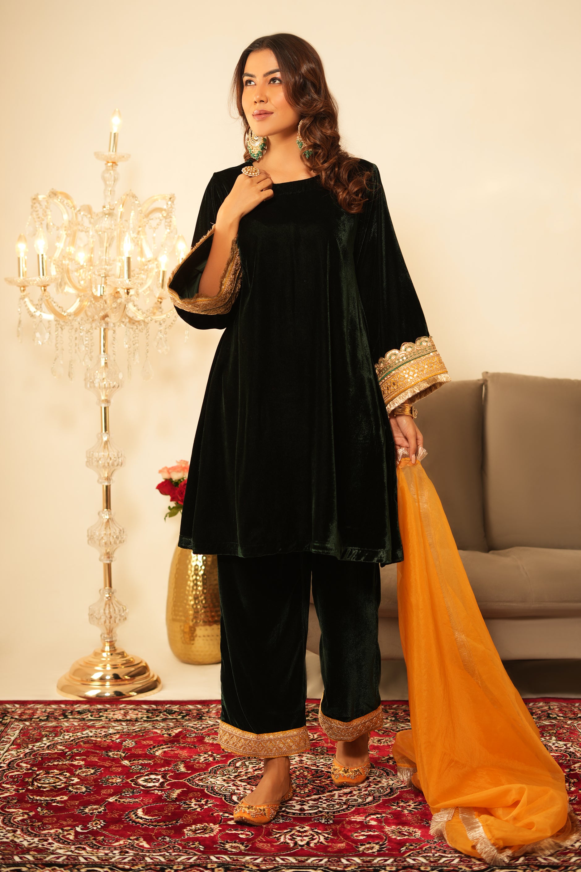 Woman wearing Green Velvet Kurta Set with Mustard Organza Dupatta featuring gota lace detailing, boat neckline, 3/4th sleeves, and matching green velvet pants with elastic waist and lace hem