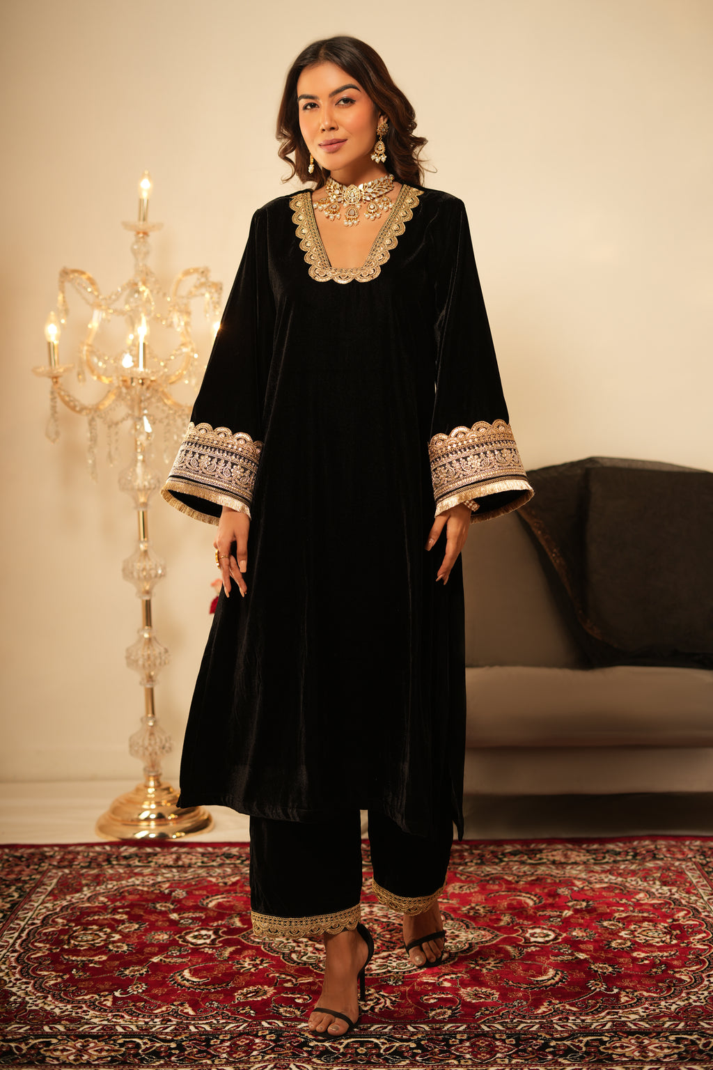 Woman wearing a black traditional outfit with gold embroidery in a decorated room.