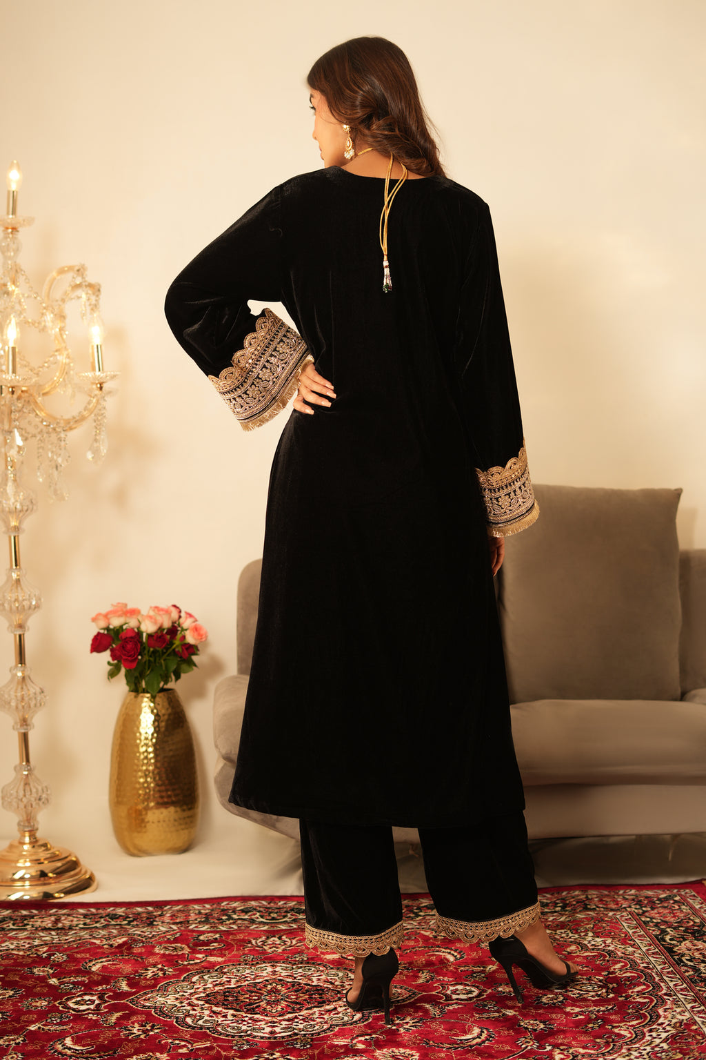 Woman wearing a black outfit with gold embroidery in a decorated room.