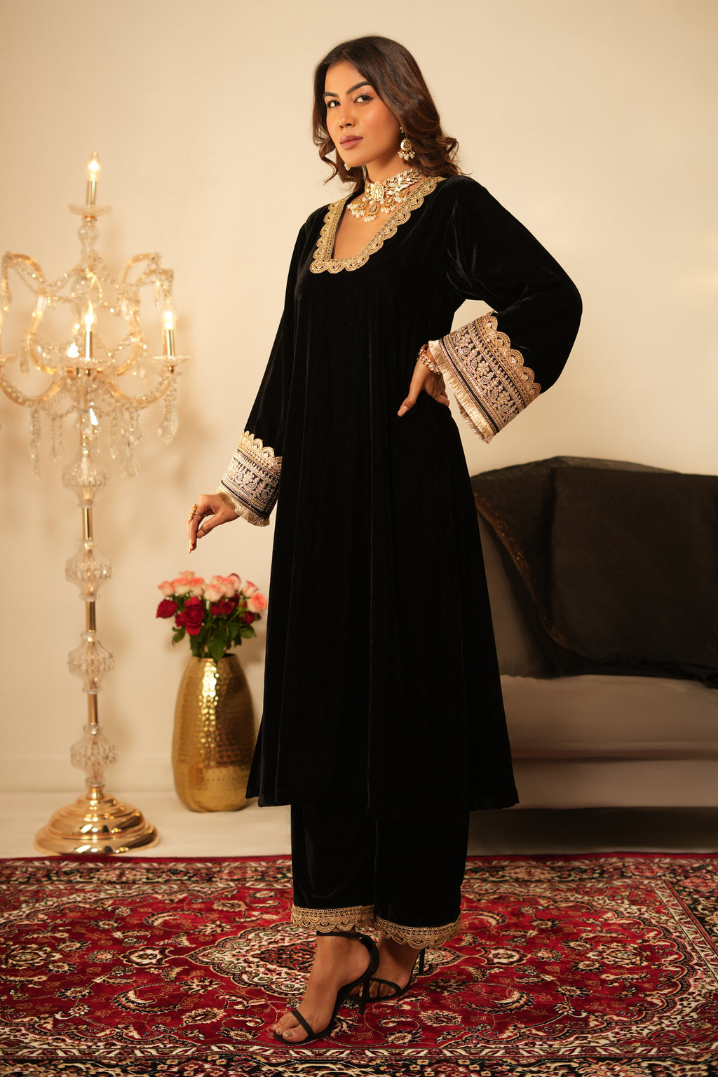 Woman in a black traditional outfit with white embroidery standing in a room with decorative elements.