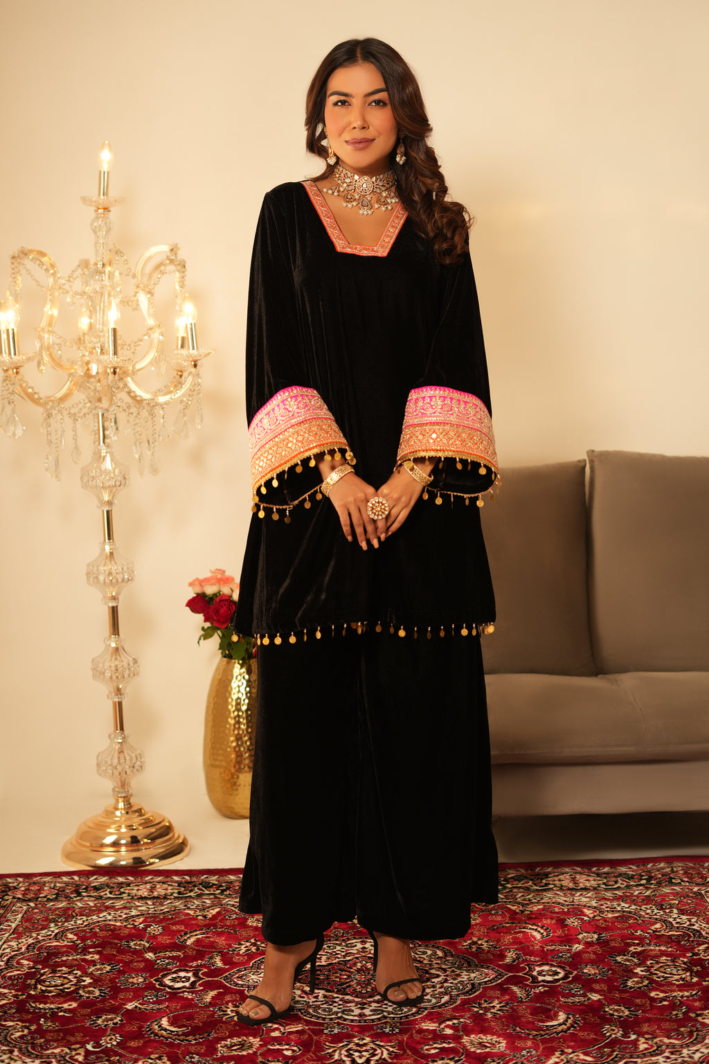 Woman in a black dress with pink accents standing in a room with a chandelier and sofa.