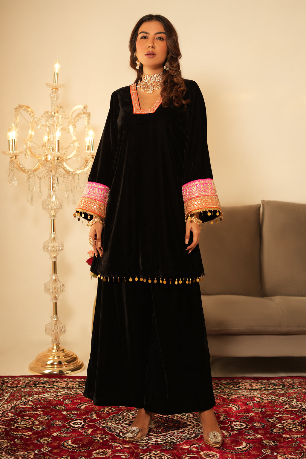 Woman in a black traditional outfit with pink and gold details standing on a patterned rug.