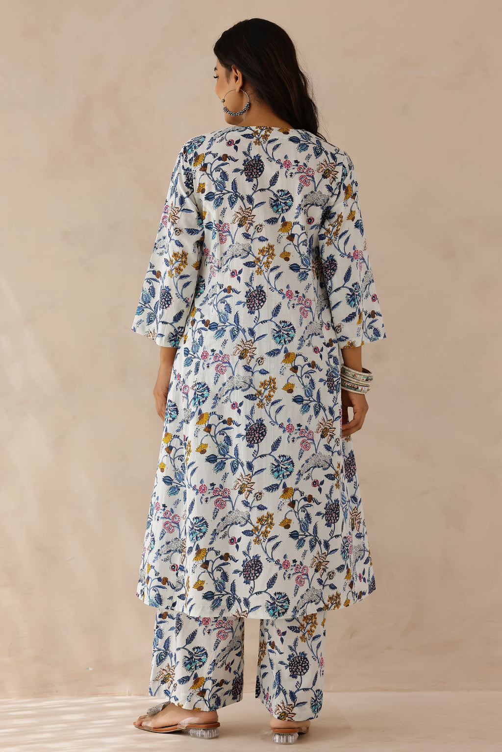 Woman wearing white printed cotton kurta with round V-cut neckline, 3/4 sleeves, and white cotton pants.