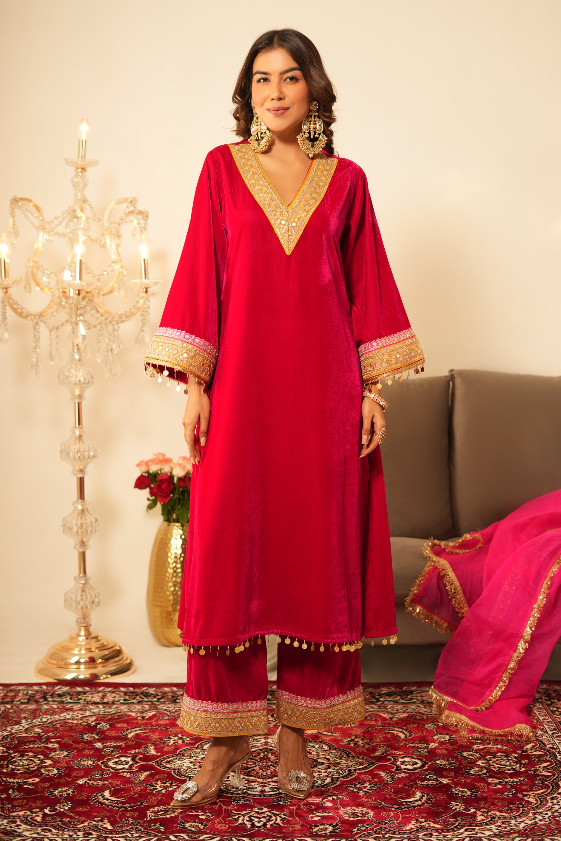Woman in a pink traditional velvet kurta with gold details standing in a decorated room.