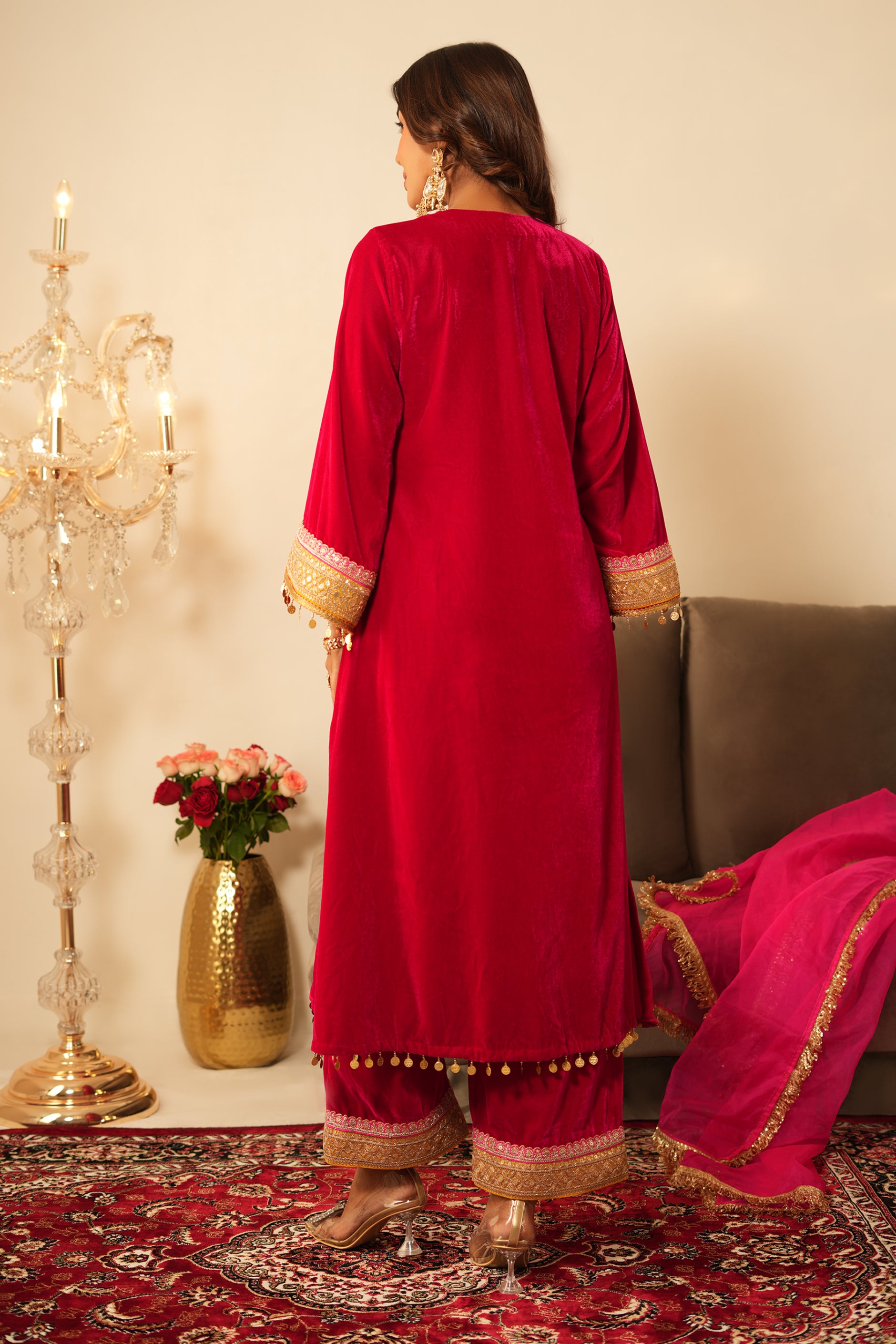 Woman in a pink traditional velvet kurta with gold details standing in a decorated room.