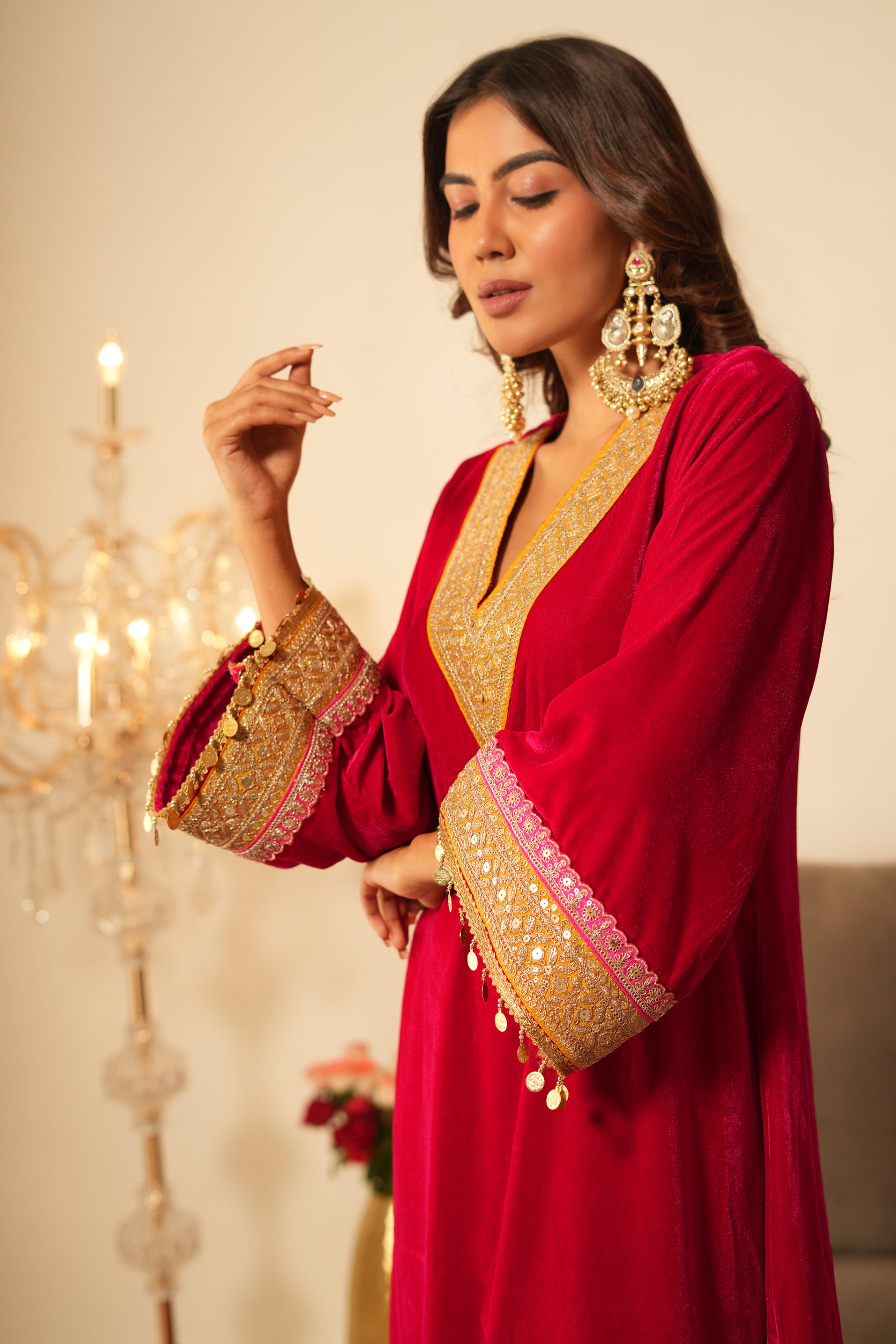 Woman in a pink traditional velvet kurta with gold details standing in a decorated room.