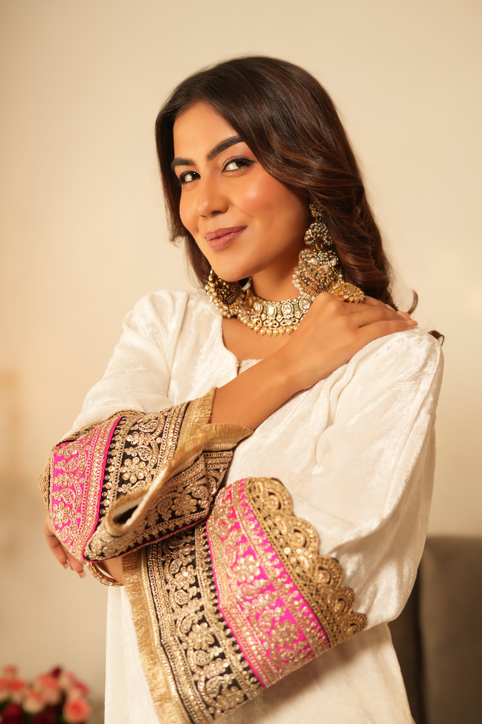 Woman in a white traditional velvet kurta with gold details standing in a decorated room with black and pink organza dupatta
