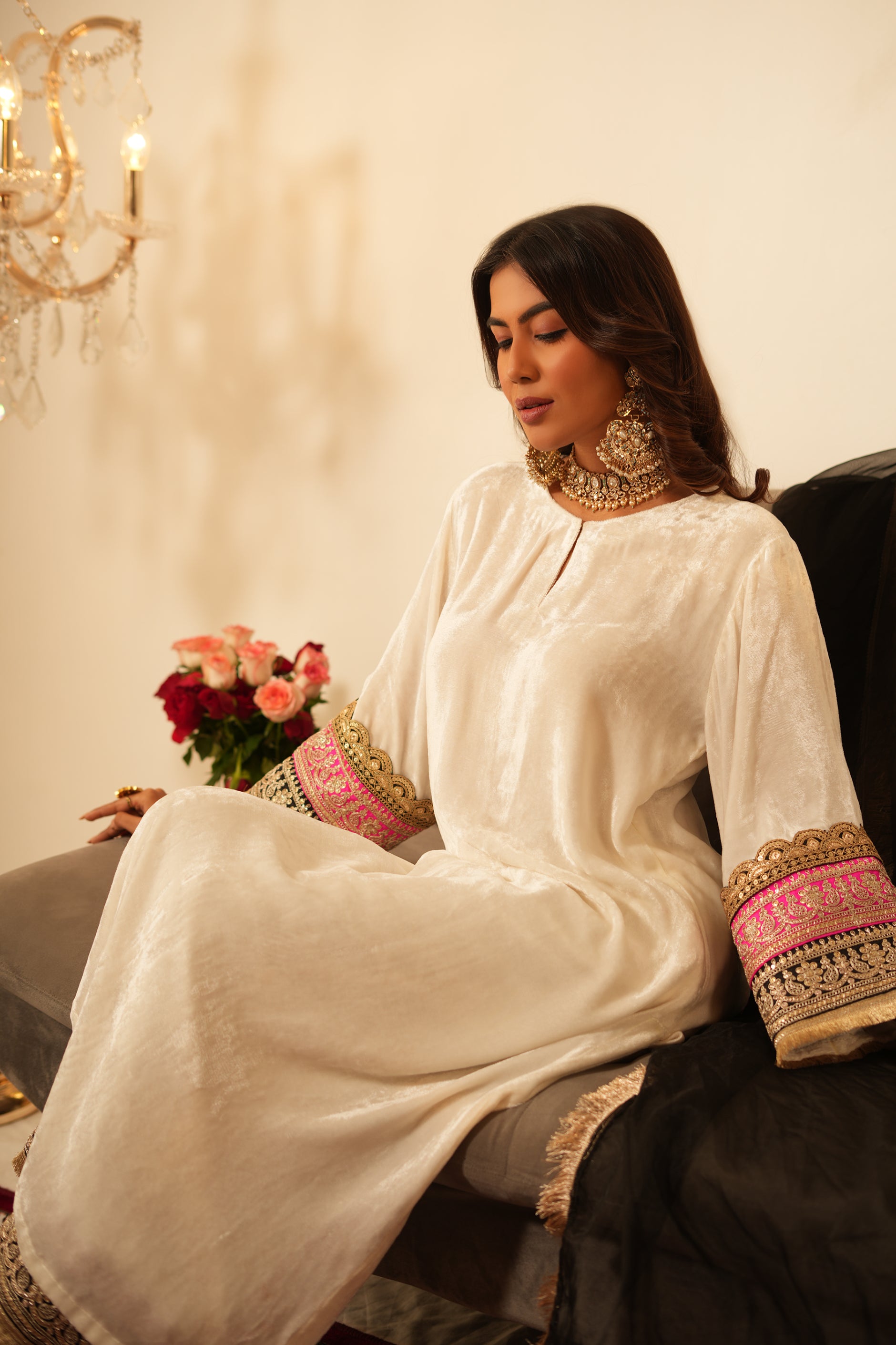 Woman in a white traditional velvet kurta with gold details standing in a decorated room with black and pink organza dupatta
