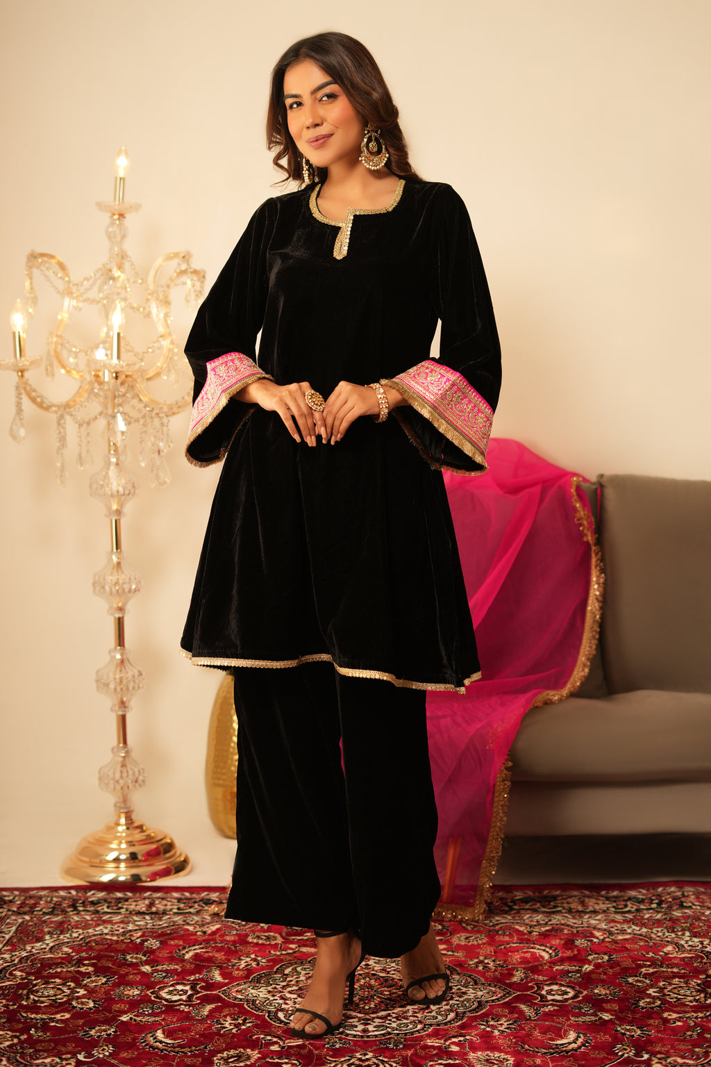 Woman in Black Gota Lace Velvet  Kurta holding a pink dupatta in a decorated room.