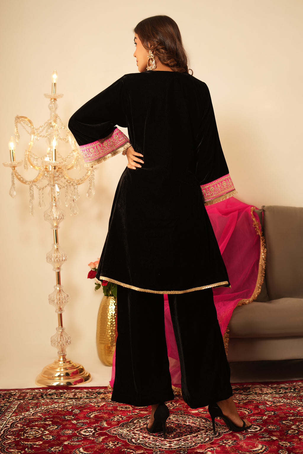 Woman in Black Gota Lace Velvet  Kurta holding a pink dupatta in a decorated room.
