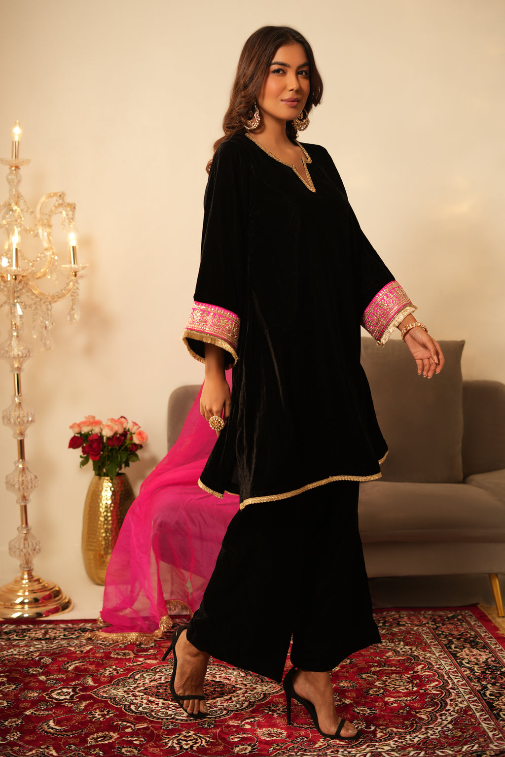 Woman in Black Gota Lace Velvet  Kurta holding a pink dupatta in a decorated room.