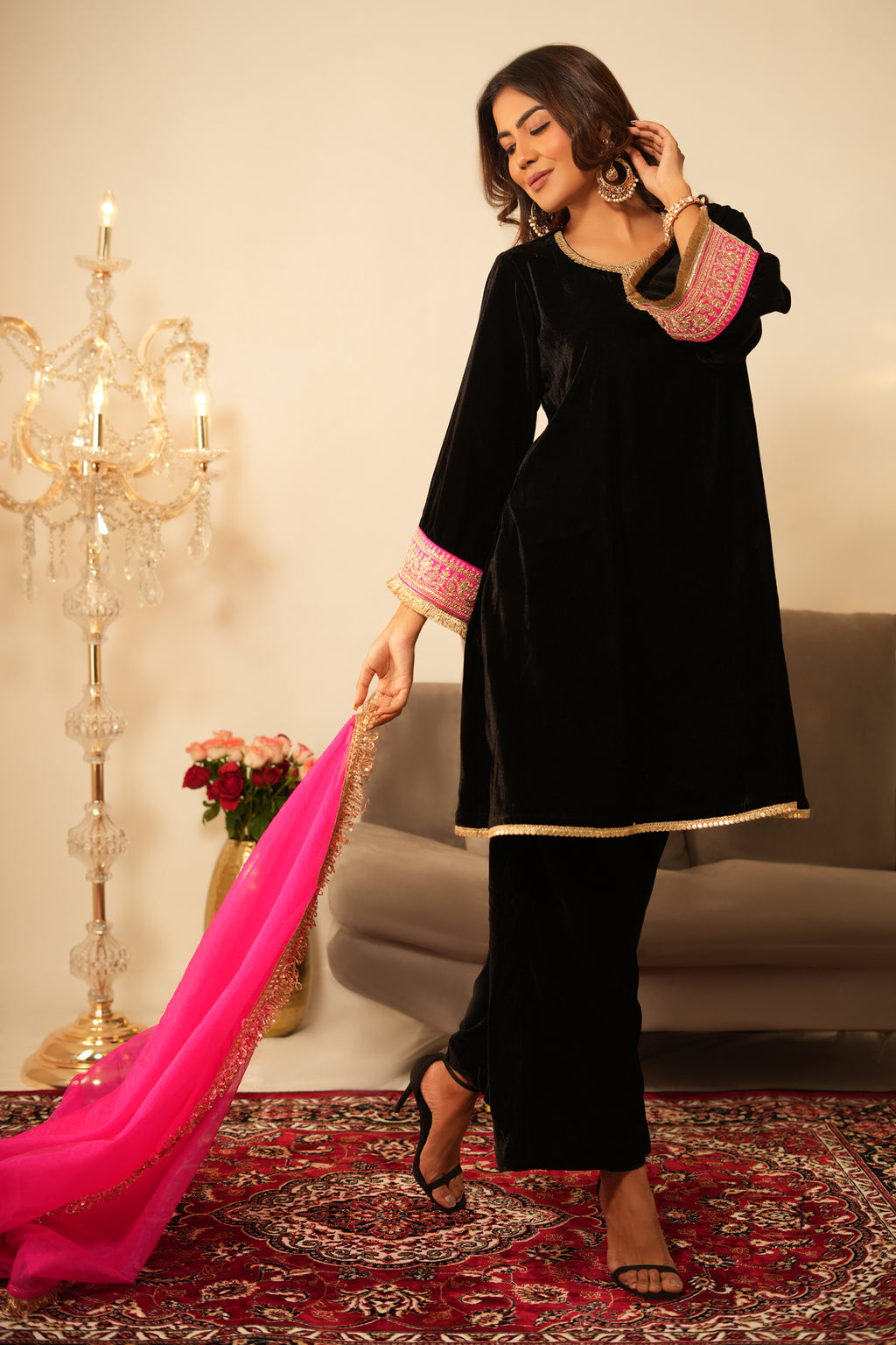 Woman in Black Gota Lace Velvet  Kurta holding a pink dupatta in a decorated room.