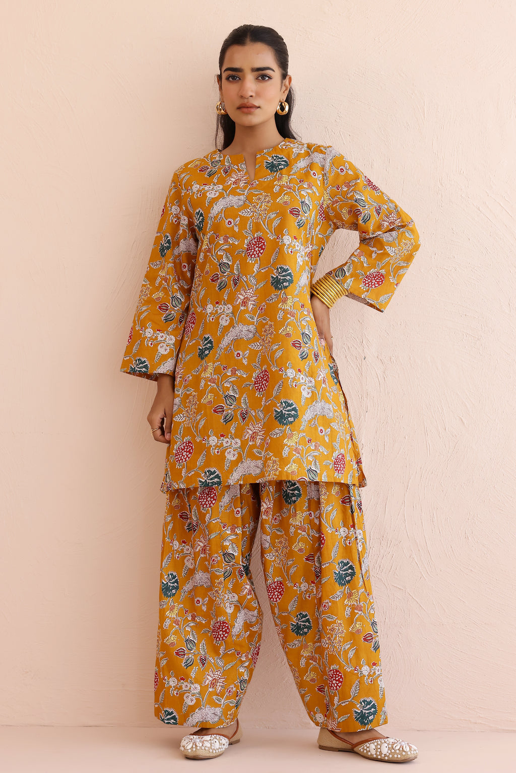 Woman wearing a mustard yellow floral kurta  with round V-cut neckline, full sleeves, and cotton pants 