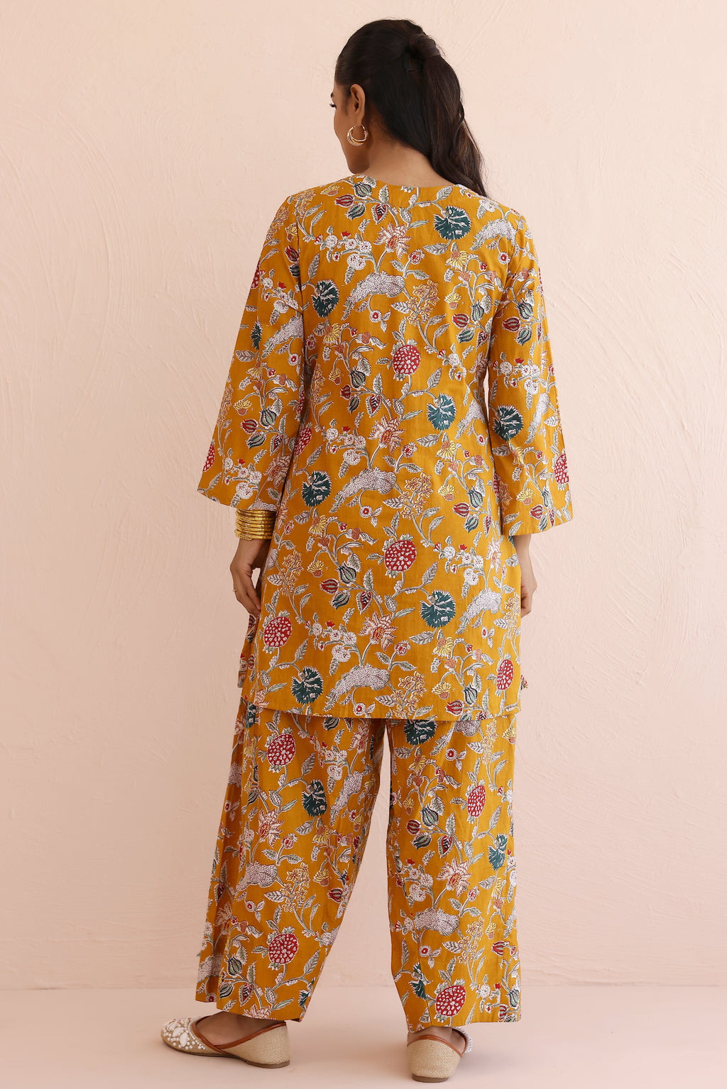 Woman wearing a mustard yellow floral kurta  with round V-cut neckline, full sleeves, and cotton pants 