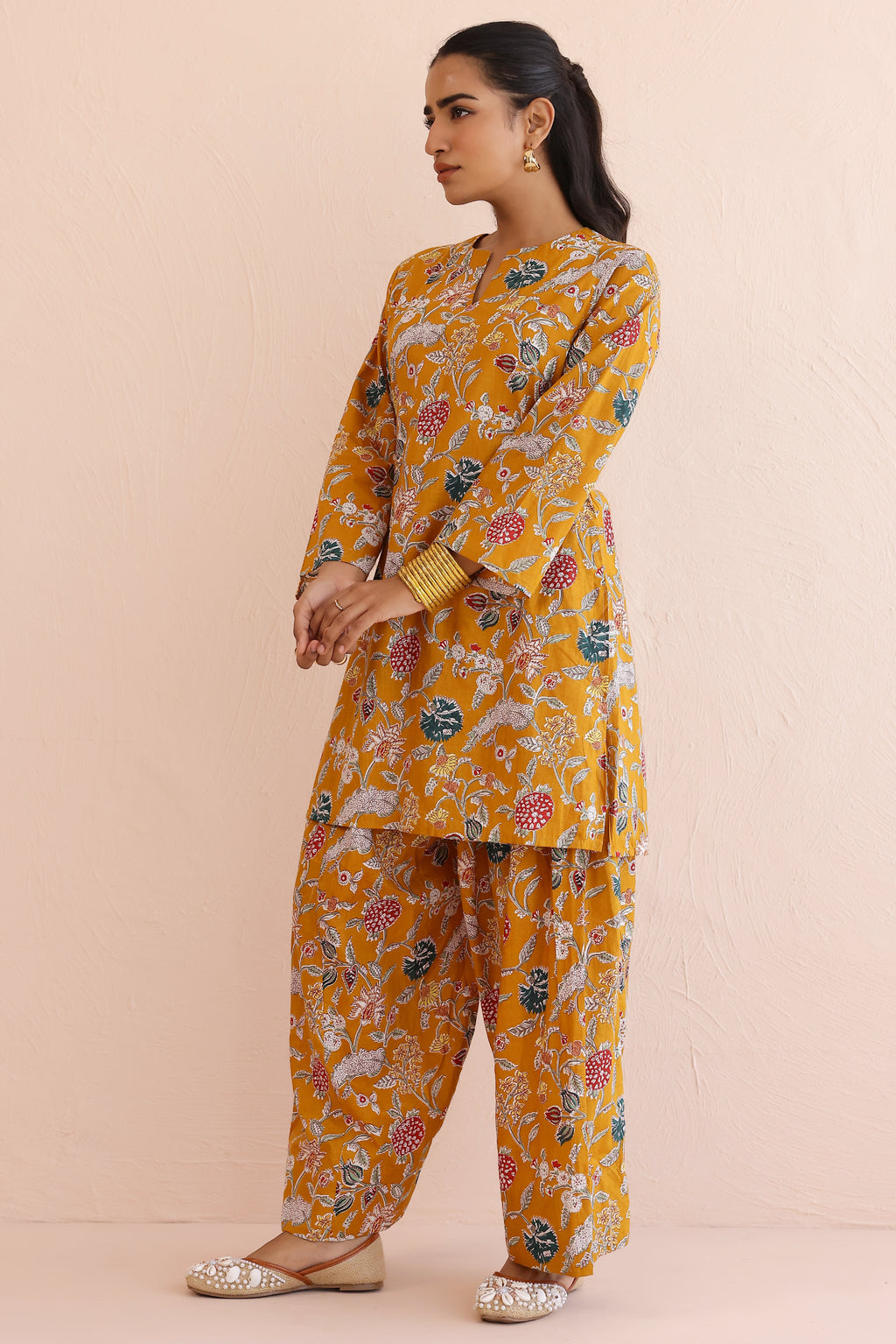 Woman wearing a mustard yellow floral kurta  with round V-cut neckline, full sleeves, and cotton pants 