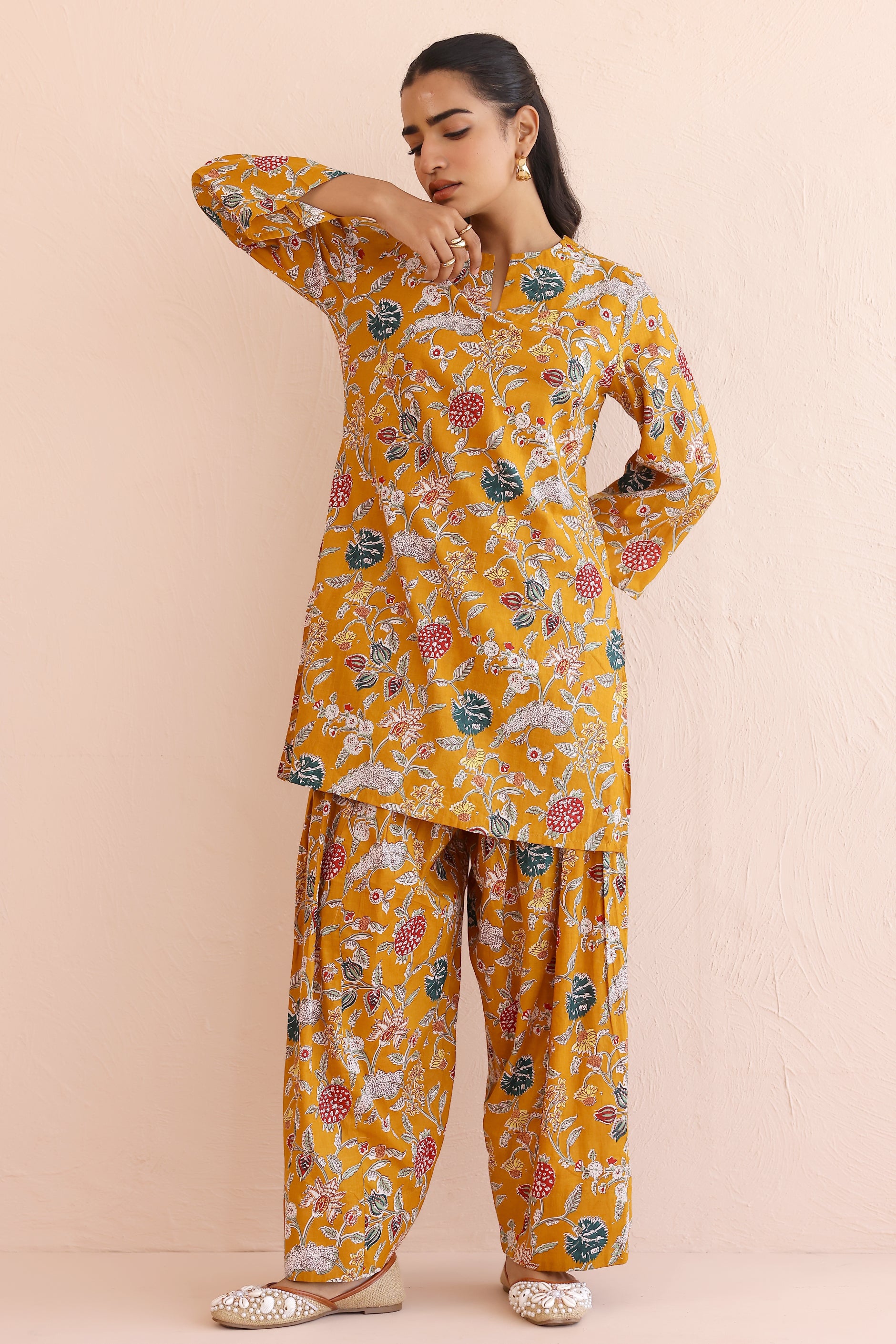 Woman wearing a mustard yellow floral kurta  with round V-cut neckline, full sleeves, and cotton pants 