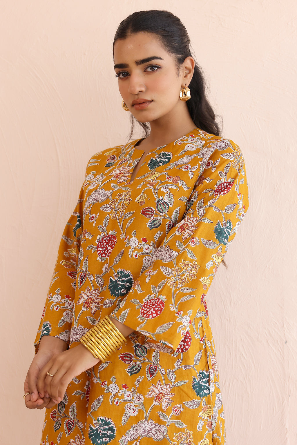 Woman wearing a mustard yellow floral kurta  with round V-cut neckline, full sleeves, and cotton pants 